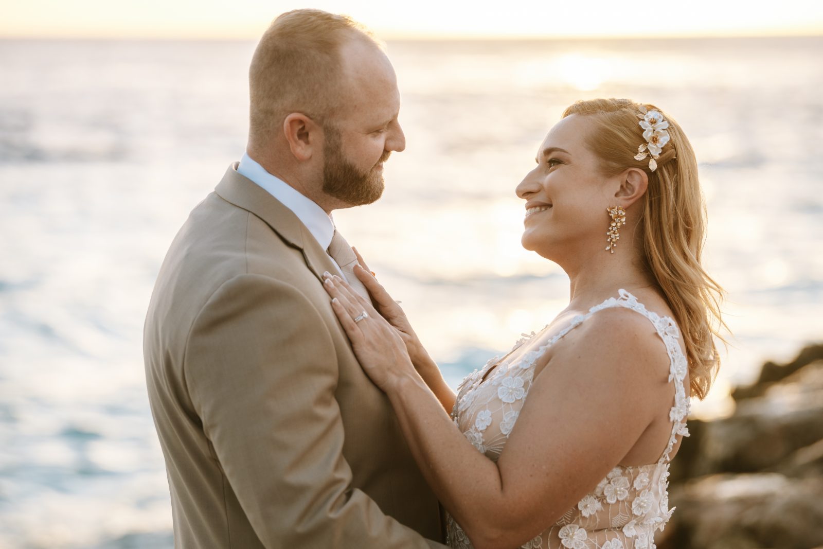 Jennifer and Weston stand close together on a rocky shoreline at sunset in Curaçao, celebrating their wedding