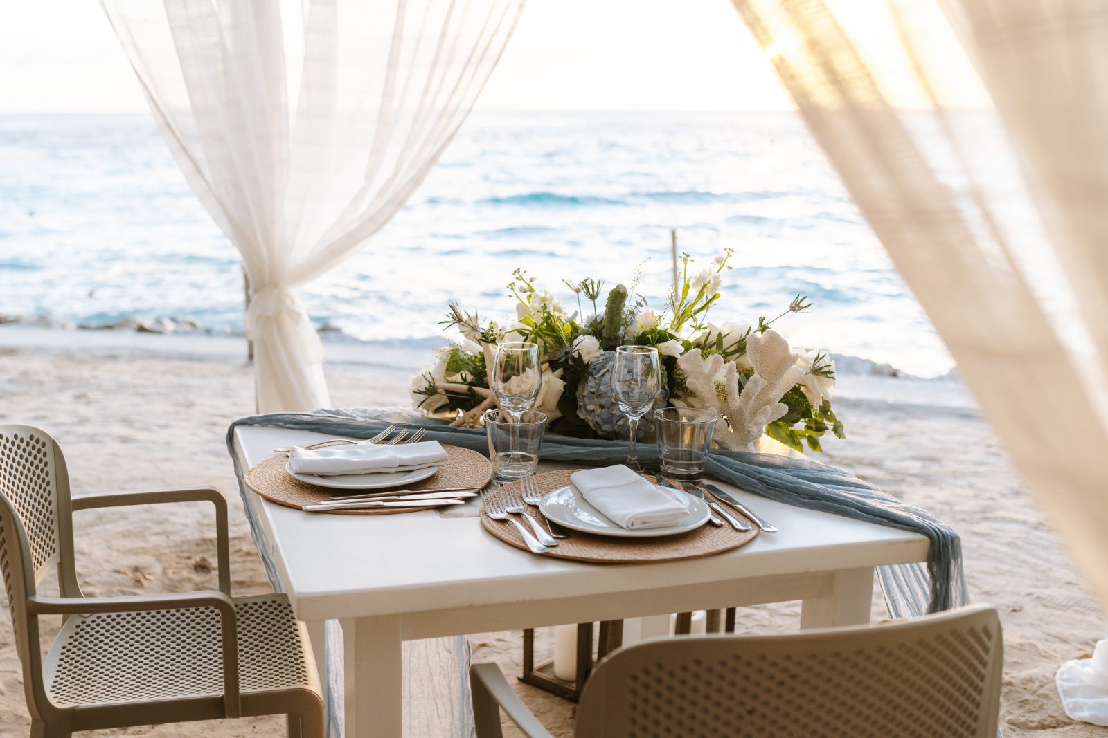 Jennifer and Weston are seated at a decorated table by the beach at Karakter in Curaçao, with an ocean view and floral centerpieces