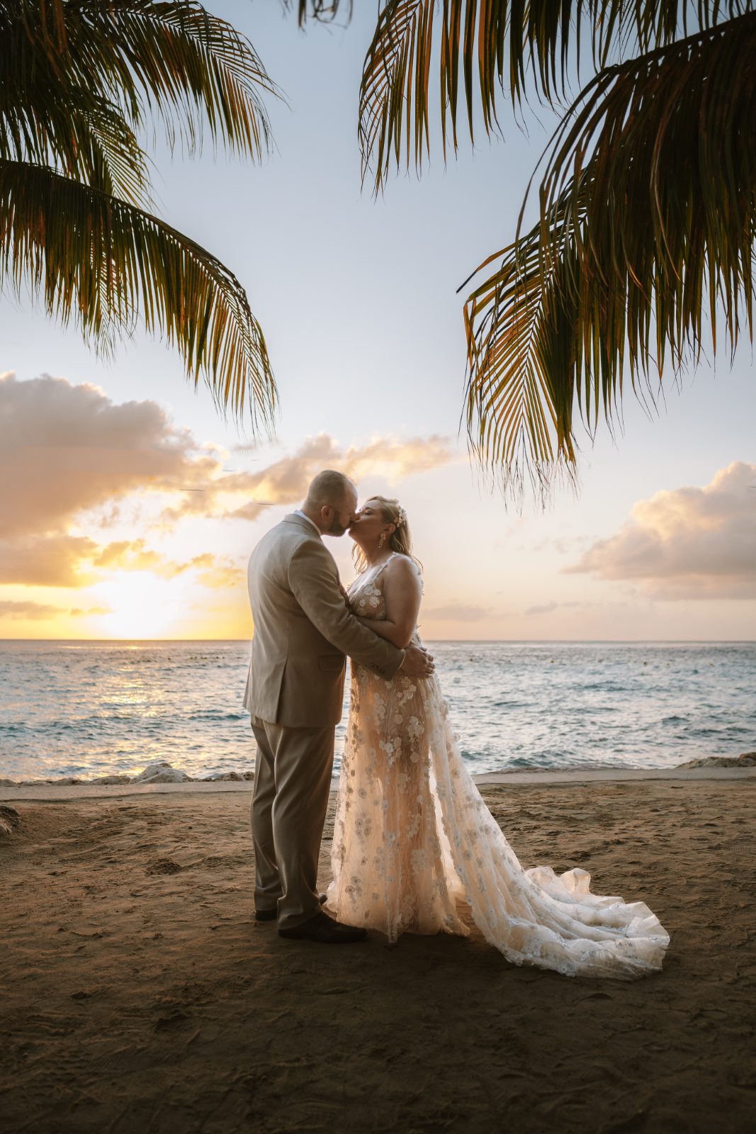 Jennifer and Weston stand together on a beach at Karakter, Curaçao, facing each other as the sun sets over the ocean behind them