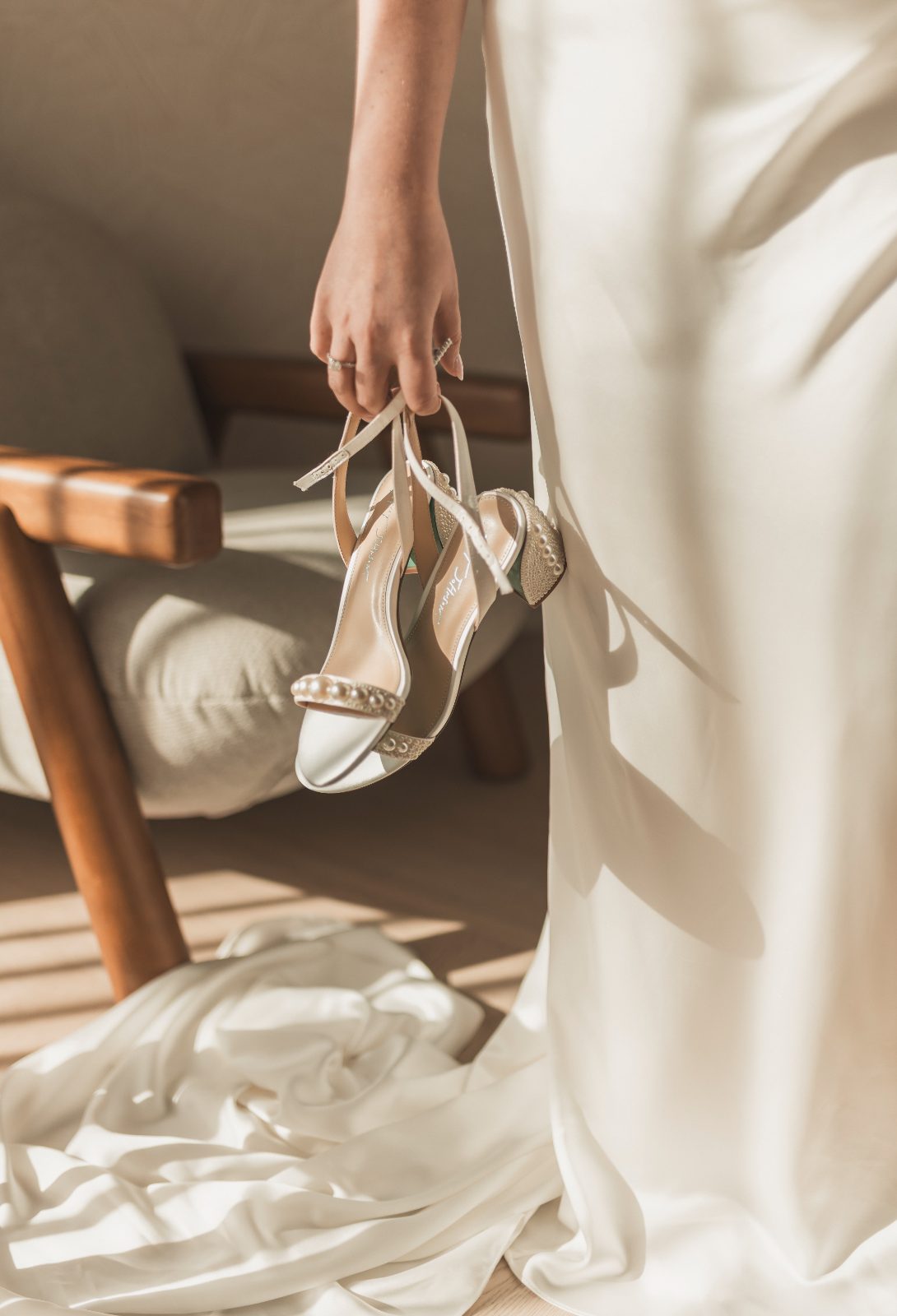 Jessica holds a pair of white shoes while standing beside a chair in her wedding dress at Avila Beach Hotel in Curaçao