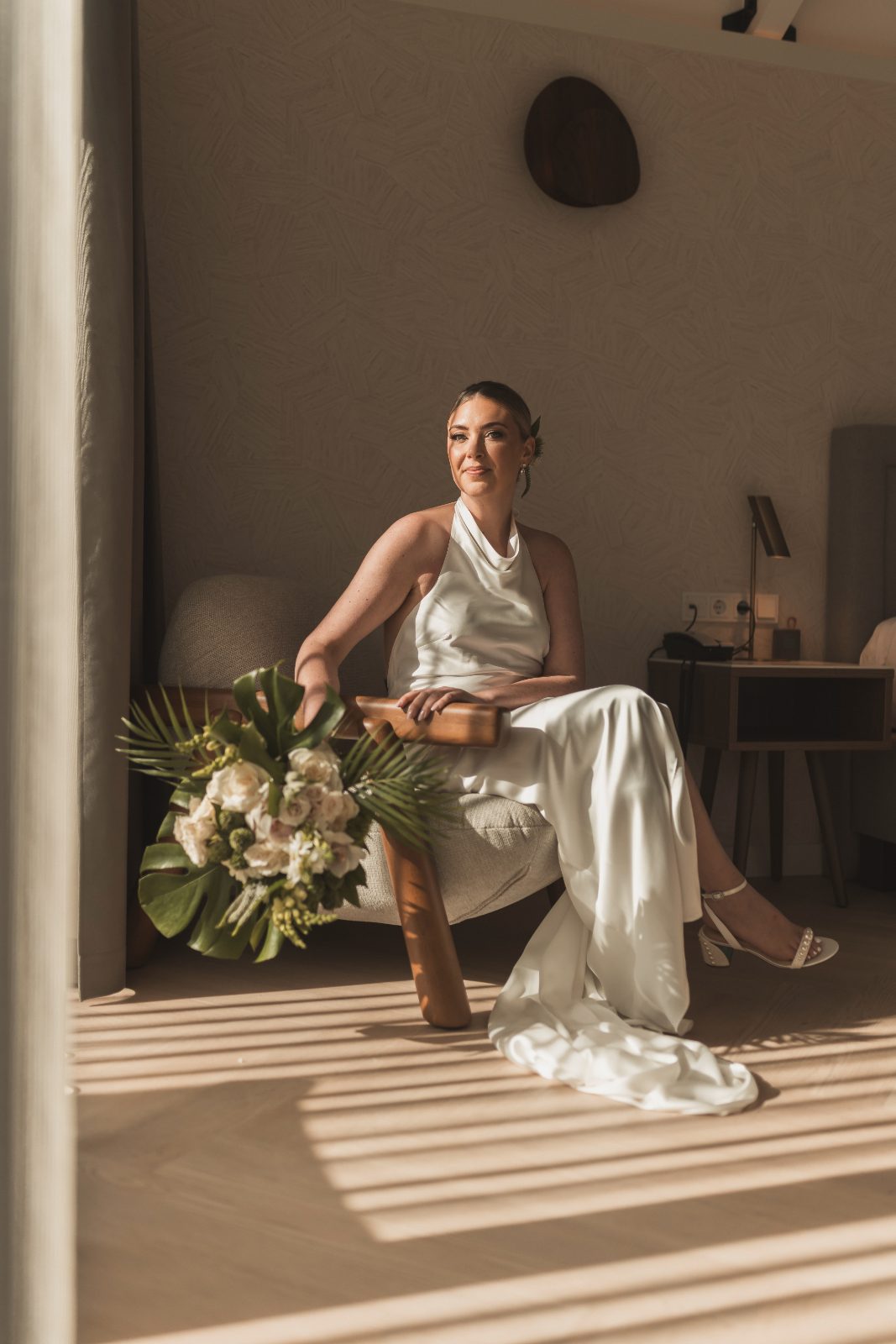 Jessica sits in a chair holding a bouquet in a softly lit room at Avila Beach Hotel, Curaçao, preparing for her wedding to Bogdan