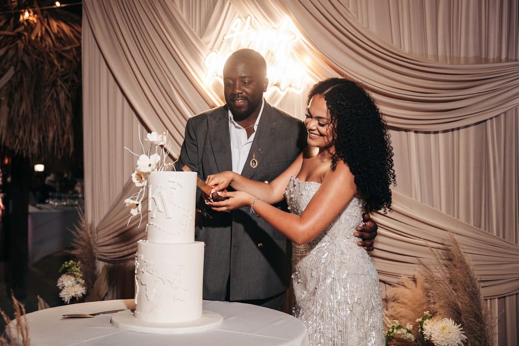 Kayla and Anthony are cutting their wedding cake at the Avila Beach Hotel, with a decorative backdrop behind them