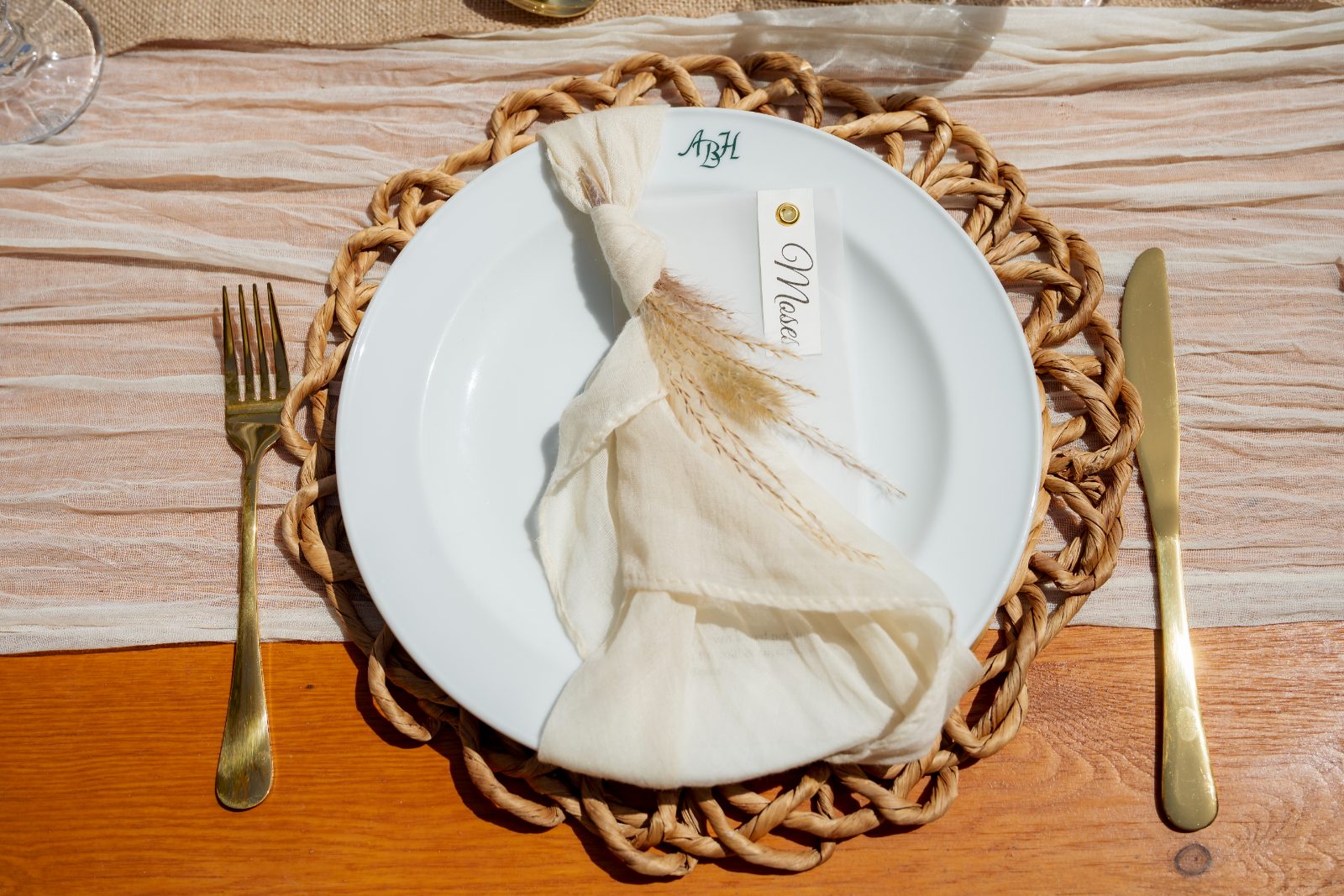 A wedding table setting at Avila Beach Hotel features a white plate with a folded napkin, a name card, and a woven placemat