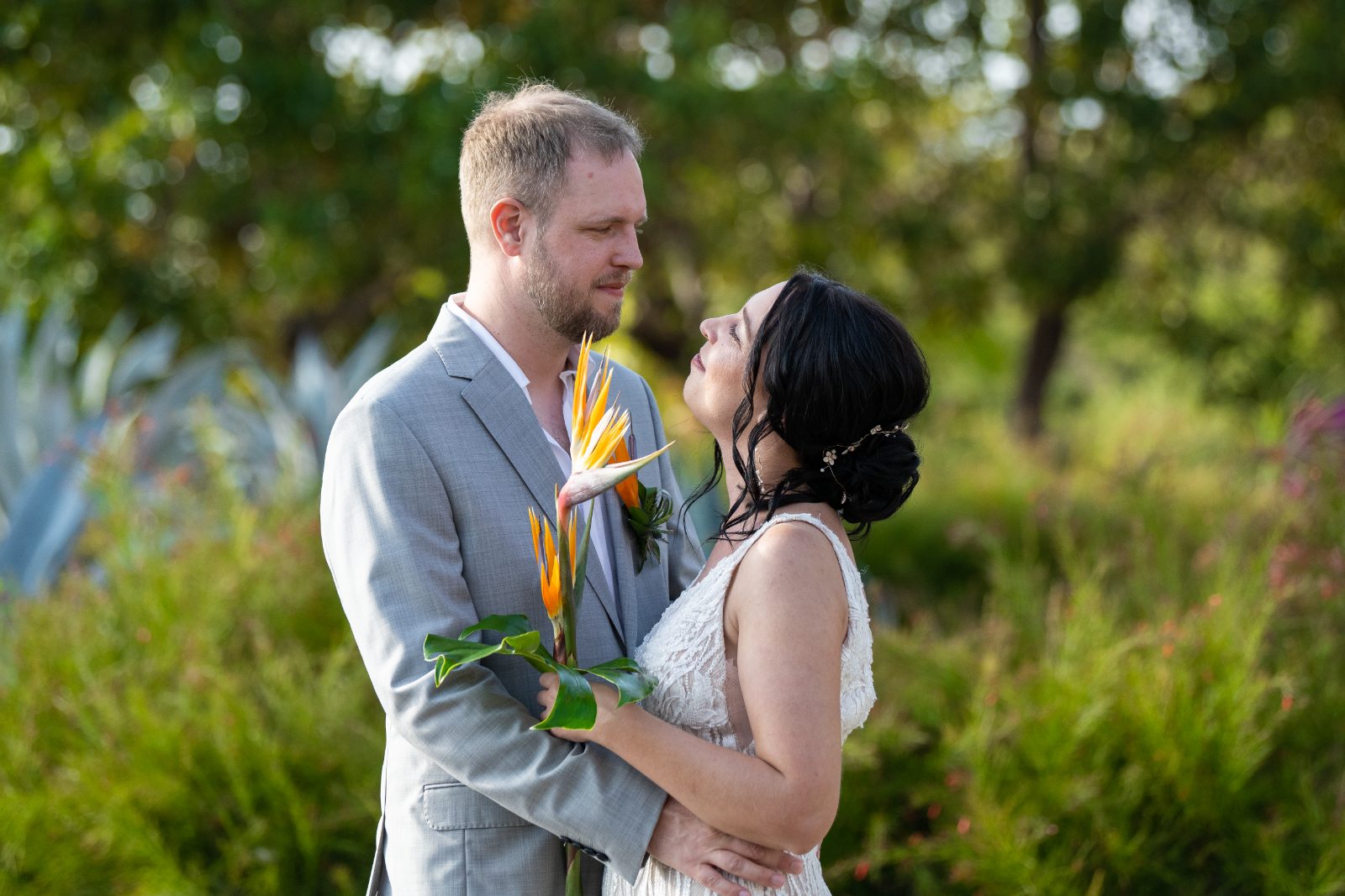Kinga and Sven stand together outdoors at Karakter, Curaçao, with lush greenery around them, as they embrace and look at each other