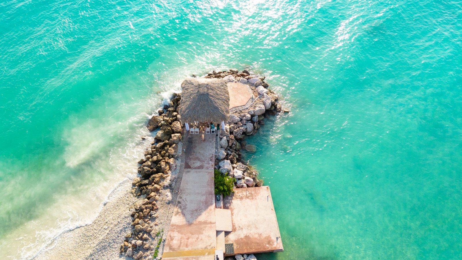 Kinga and Sven are at their wedding ceremony on a rocky pier surrounded by turquoise waters at Karakter, Curaçao