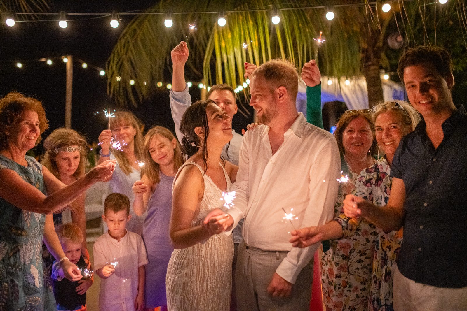 Kinga and Sven celebrate their wedding at Karakter, Curaçao, surrounded by friends and family holding sparklers in a festive evening setting