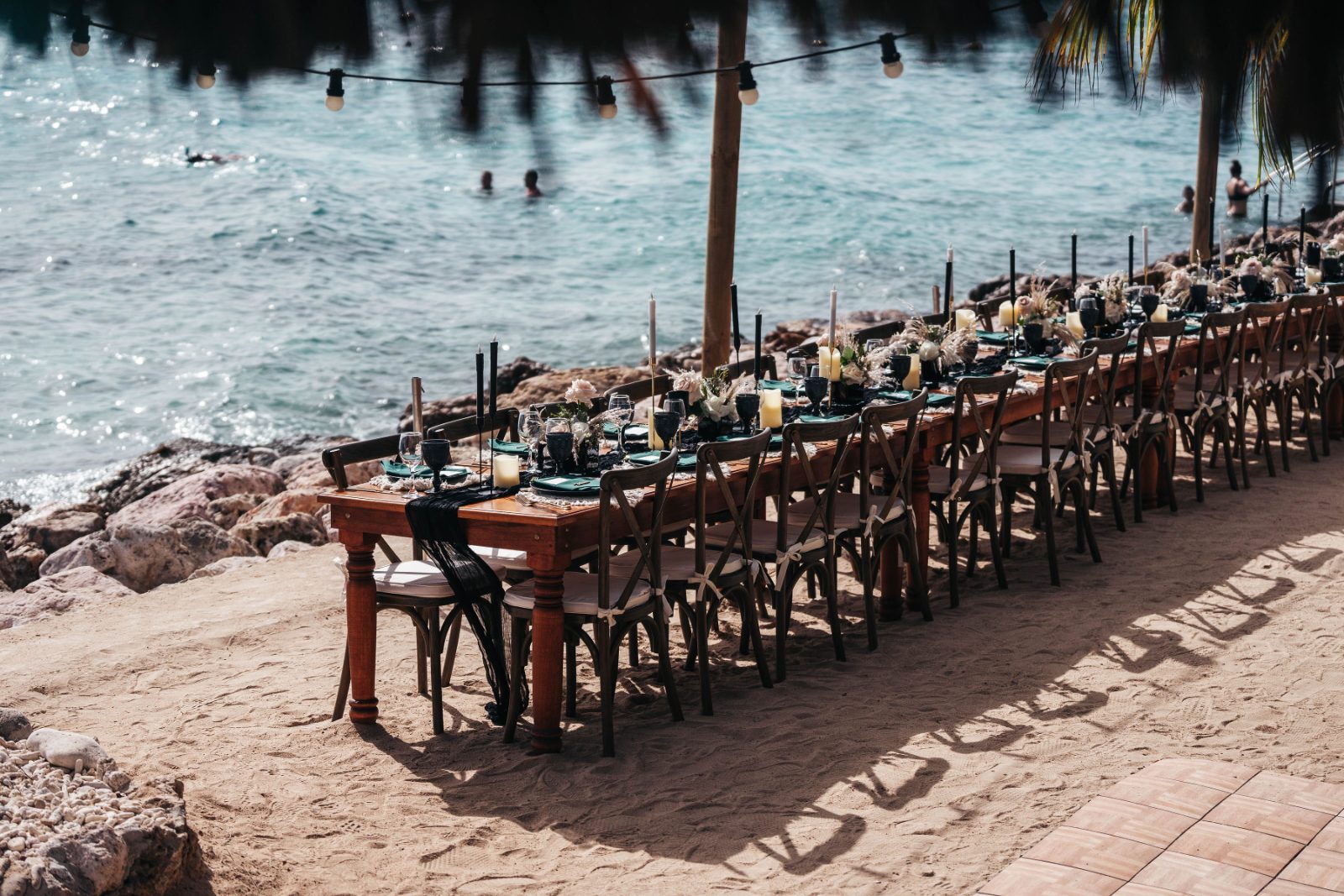 Kristal and Brittany's wedding setup features a long table decorated with candles and flowers at Karakter, Curaçao, near the ocean
