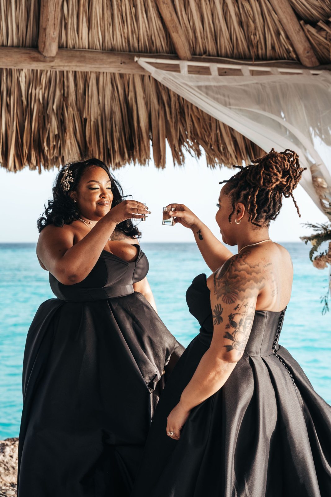 Kristal and Brittany toast with shot glasses while wearing black dresses near the water at Karakter in Curaçao