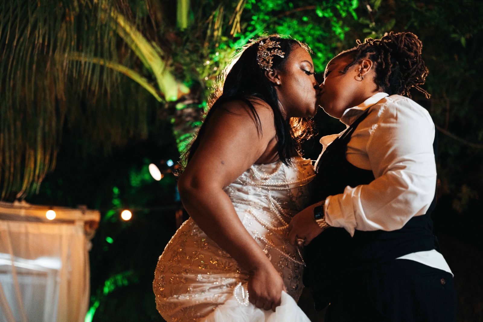 Kristal and Brittany are kissing during their wedding ceremony at Karakter in Curaçao, surrounded by tropical greenery and soft lighting