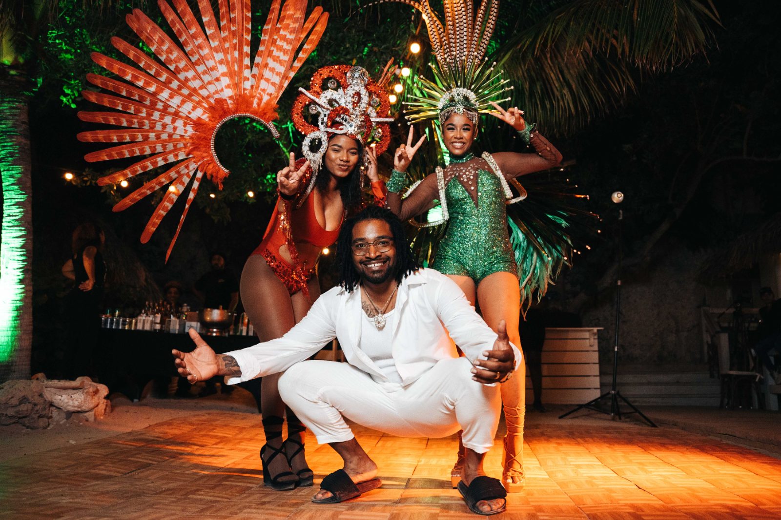 Kristal and Brittany celebrate their wedding at Karakter, Curaçao, posing with two performers in colorful costumes in front of festive decorations