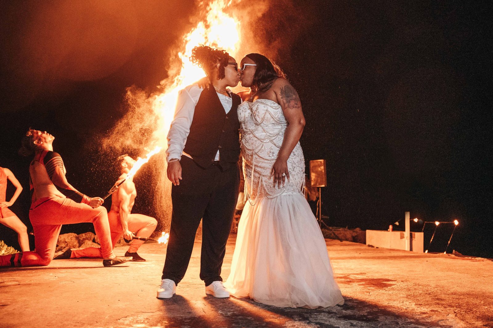 Kristal and Brittany kiss in front of a fire performance at their wedding in Karakter, Curaçao, while others perform behind them