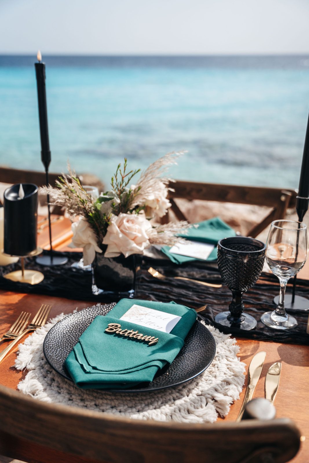 Kristal and Brittany's wedding table is set at Karakter in Curaçao, featuring a teal napkin, floral centerpiece, and ocean views