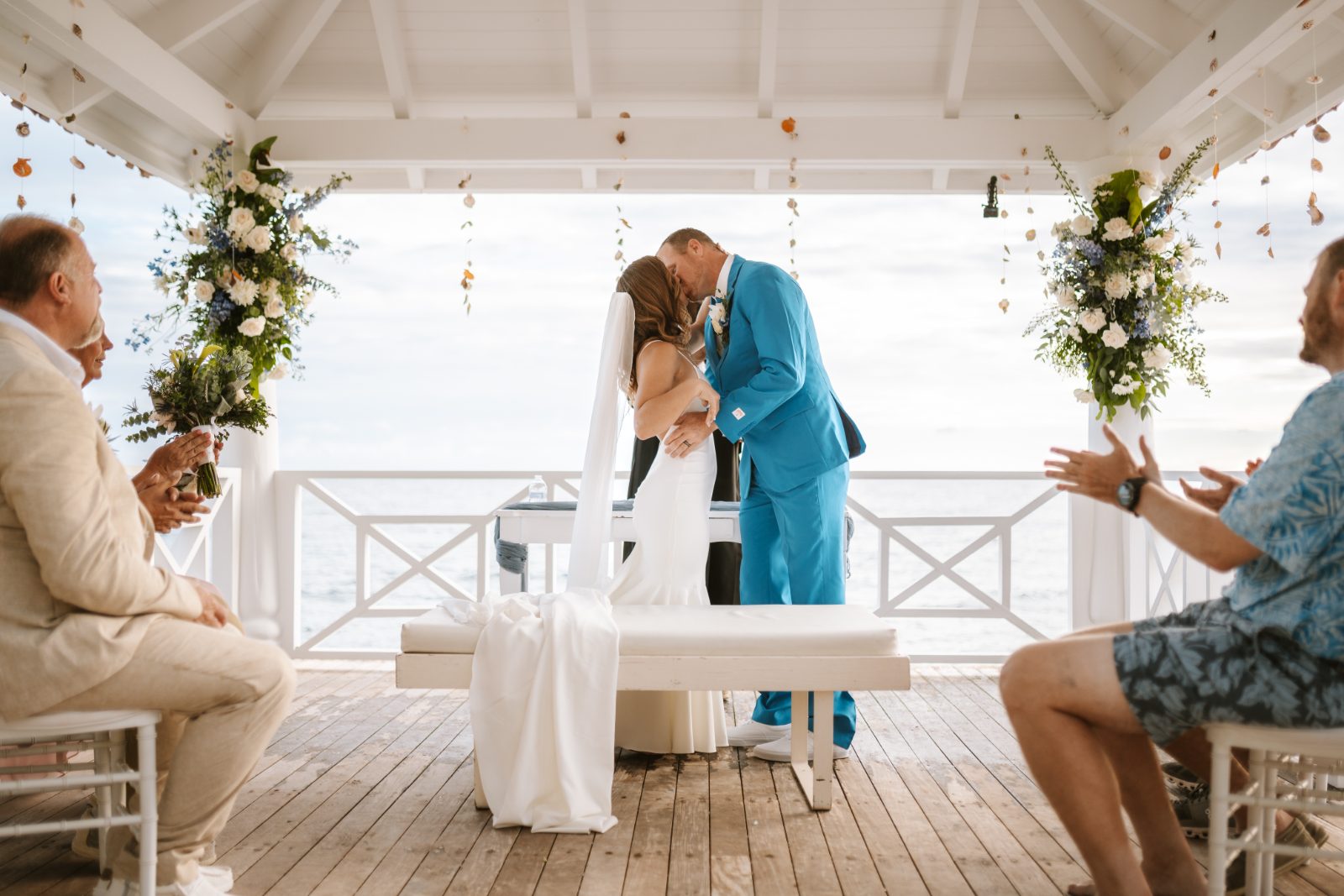 Megan and Nathan are kissing under a gazebo at their wedding in Curaçao, with guests seated and applauding nearby