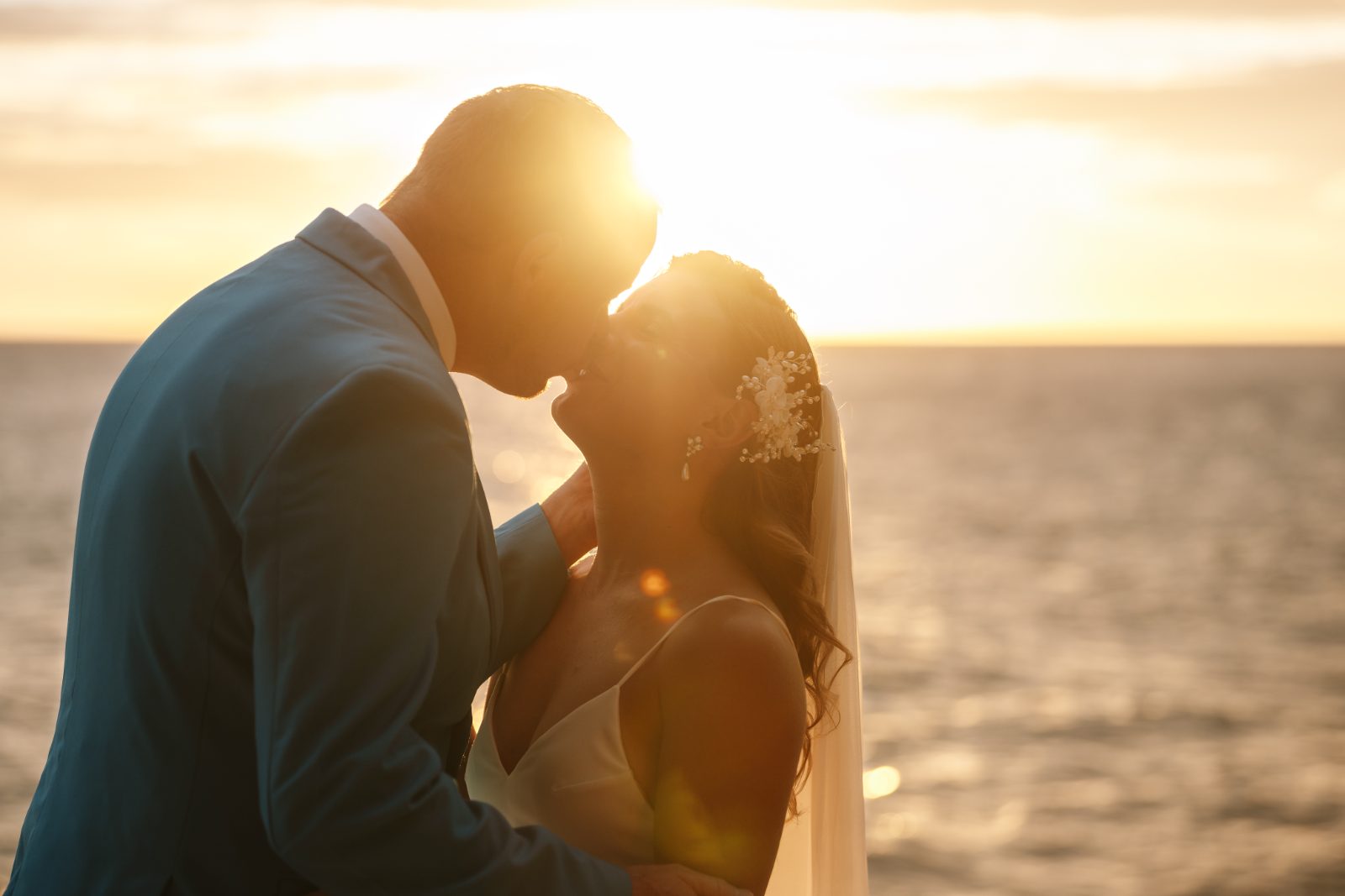 Megan and Nathan kiss against a sunset backdrop by the sea in Curaçao