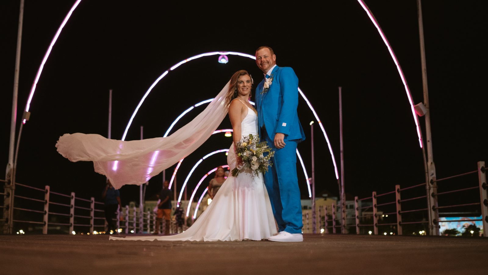 Megan and Nathan stand together on a lit walkway in Curaçao, with colorful arches in the background at night
