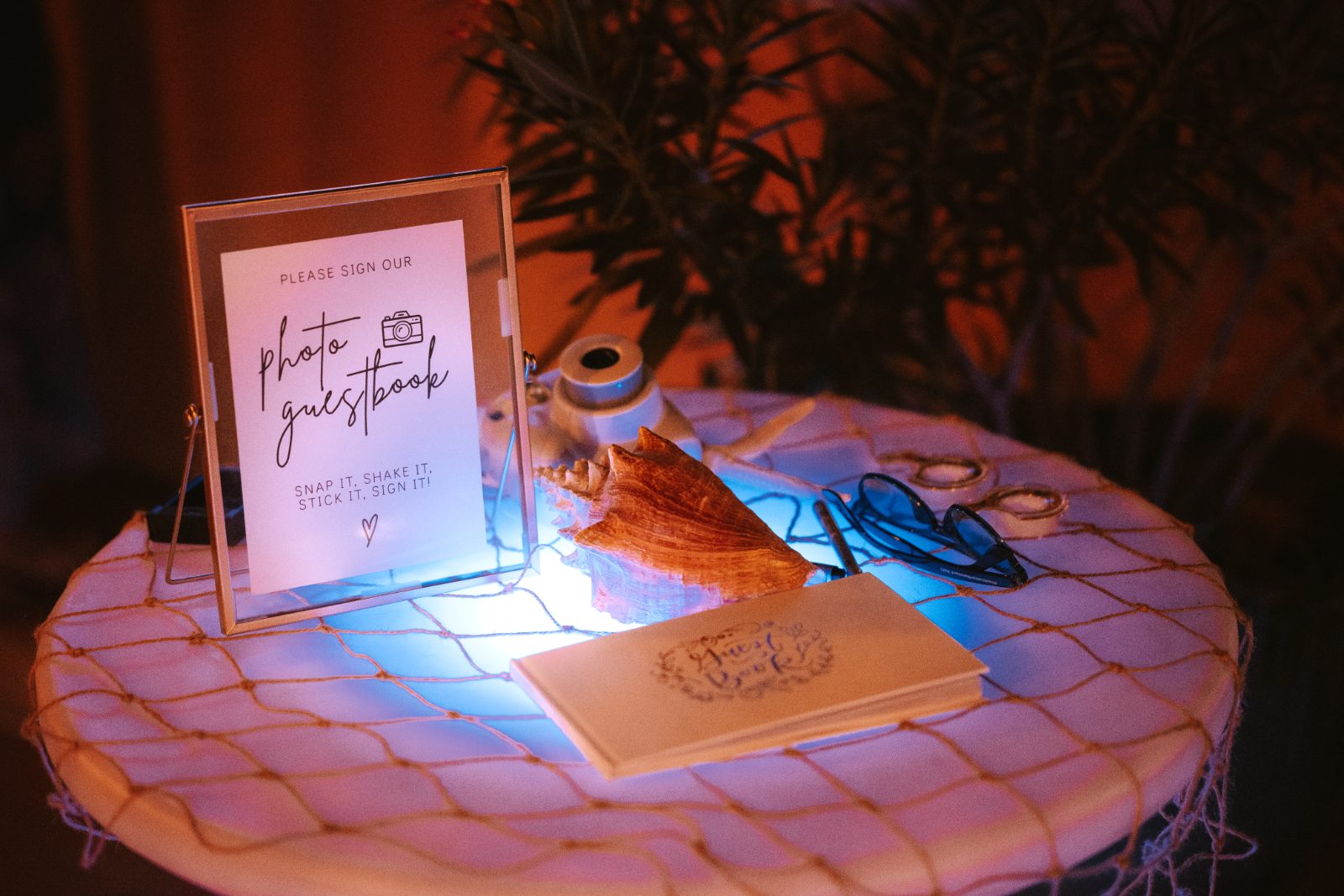 Megan and Nathan's wedding guestbook setup is displayed on a small table in Curaçao, featuring a sign, a shell, and decorative items