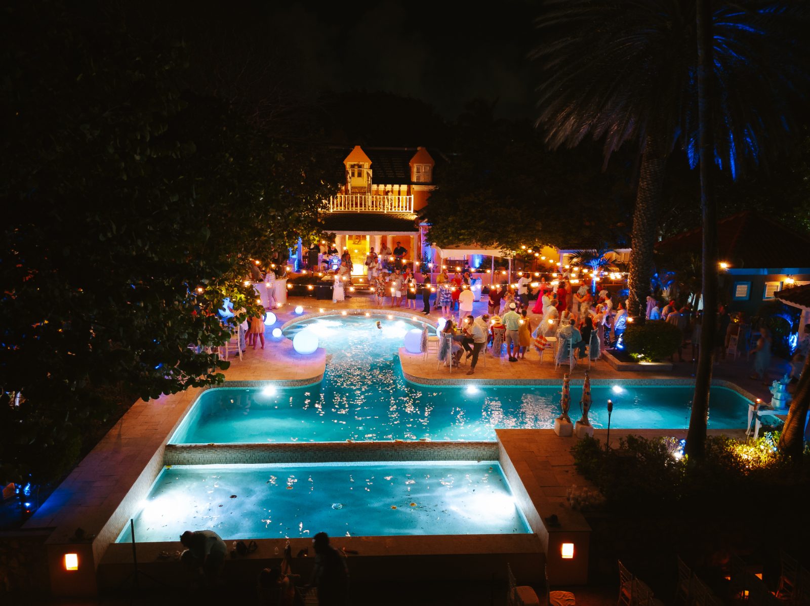 Megan and Nathan celebrate their wedding at night by a poolside venue in Curaçao, surrounded by guests enjoying the festivities