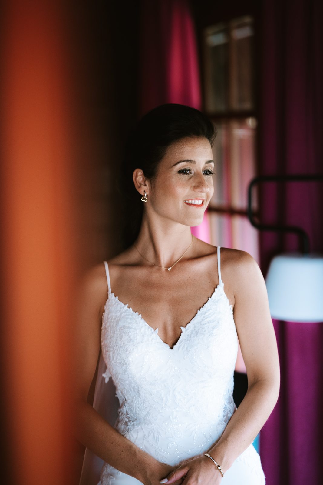 Sharon stands smiling in her wedding dress inside a venue at MOOD Beach in Curaçao, with colorful curtains in the background