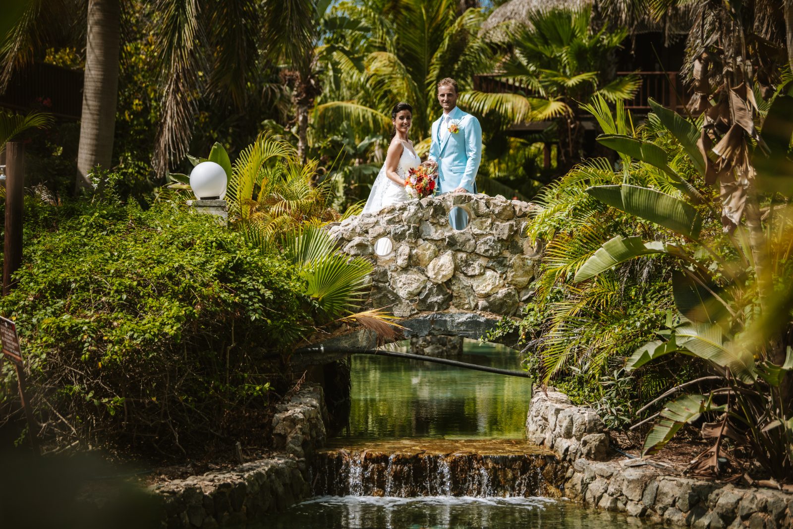 Sharon and Robin stand on a stone bridge over a small stream surrounded by tropical plants at MOOD Beach in Curaçao