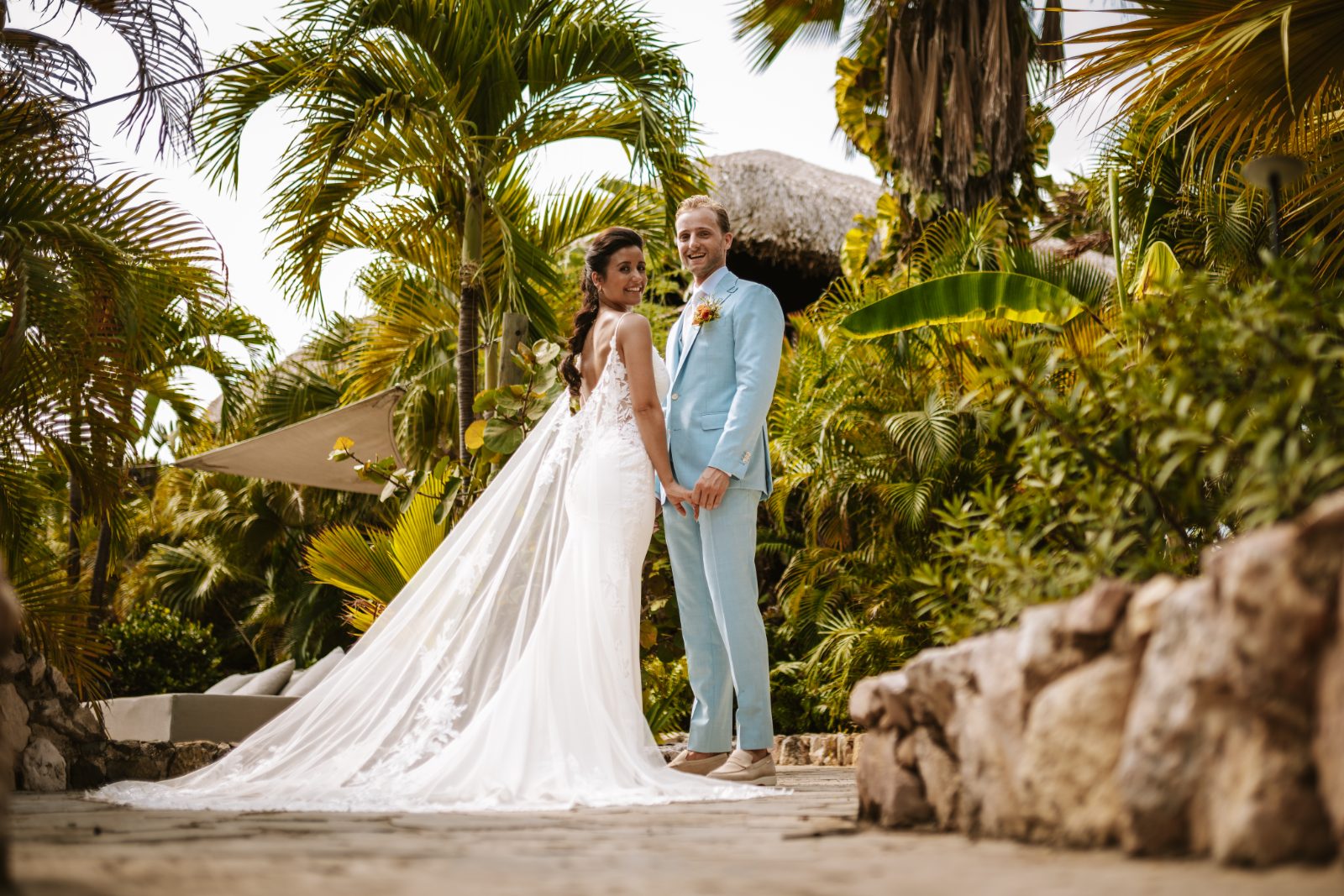 Sharon and Robin stand hand in hand at MOOD Beach in Curaçao, surrounded by tropical plants and a stone pathway