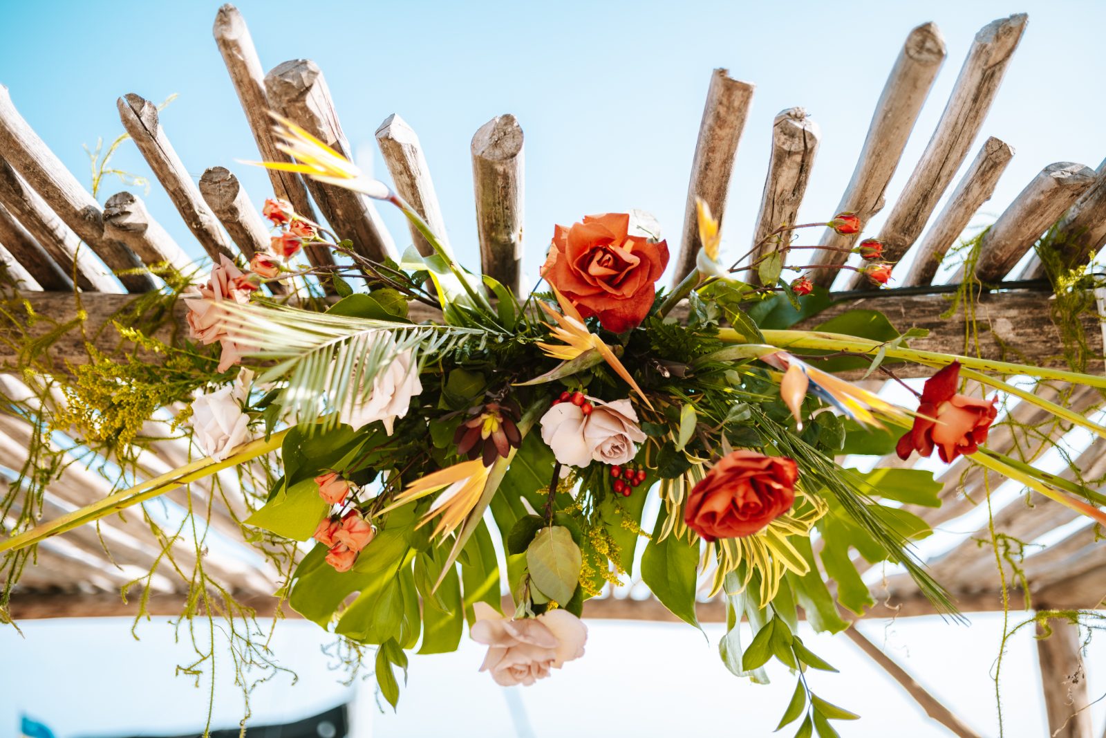 Sharon and Robin's wedding at MOOD Beach, Curaçao features a floral arrangement hanging over a wooden structure in a sunny outdoor setting