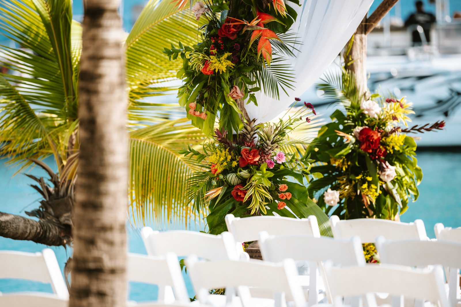 Sharon and Robin are getting married at MOOD Beach in Curaçao, surrounded by floral decorations and white chairs set up for the ceremony
