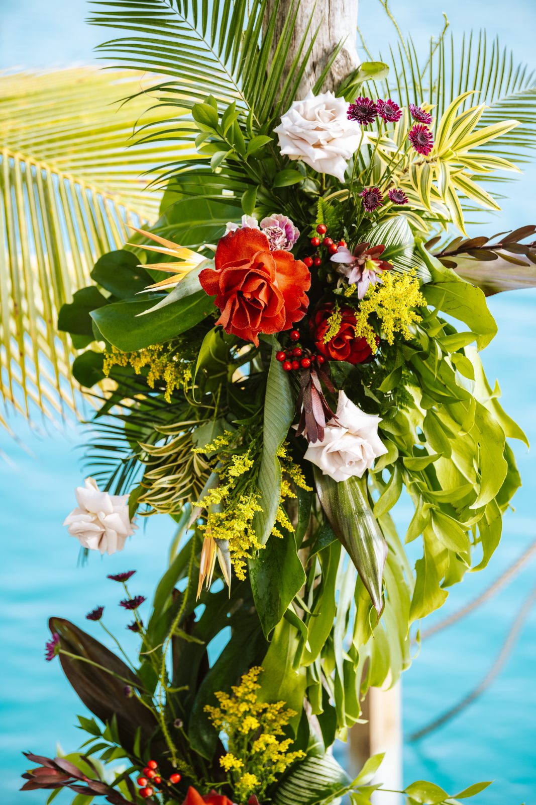 Sharon and Robin are standing under a floral arch at MOOD Beach in Curaçao during their wedding ceremony by the water
