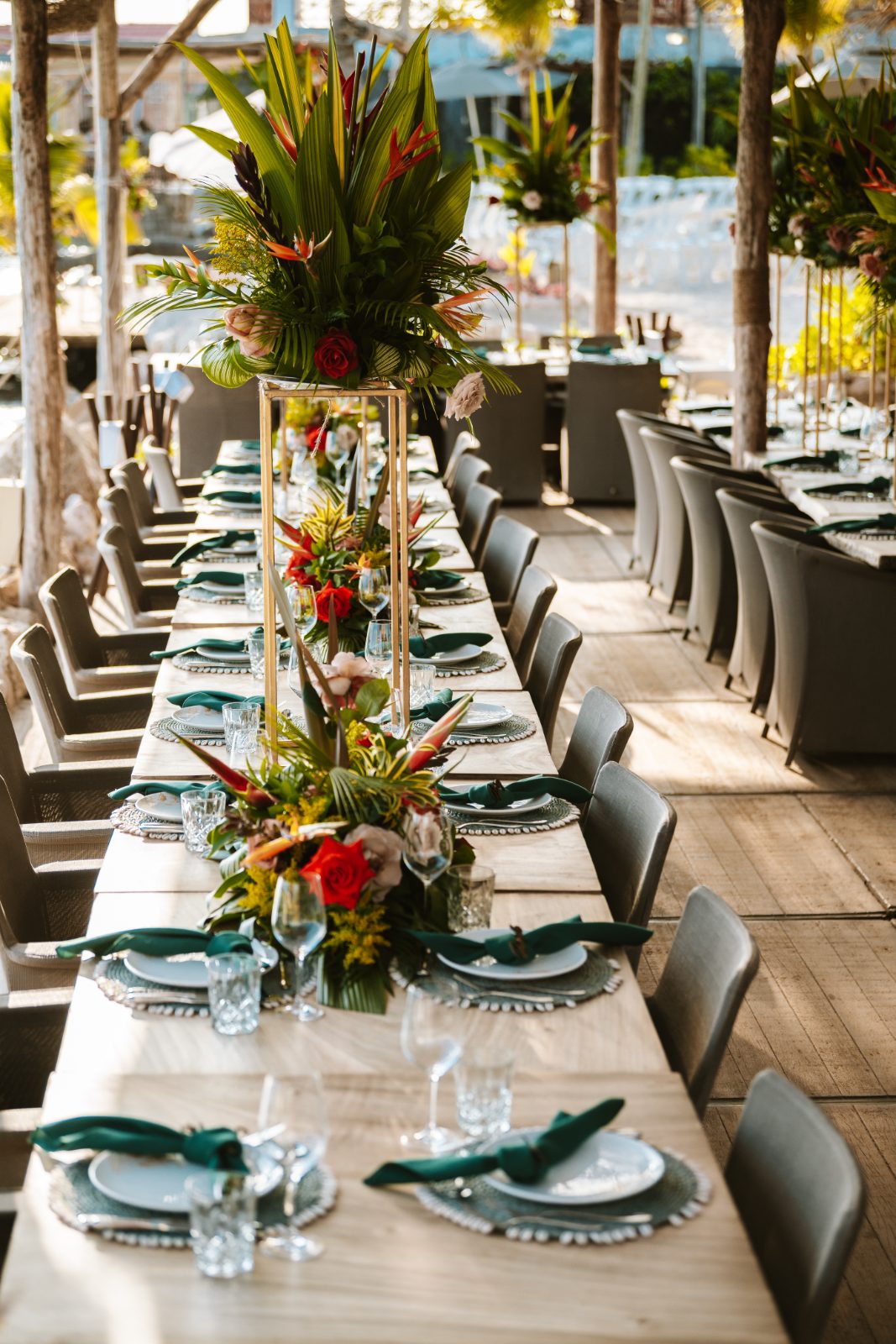 Sharon and Robin’s wedding reception features a long table decorated with floral arrangements and set under a beachside pavilion at MOOD Beach, Curaçao