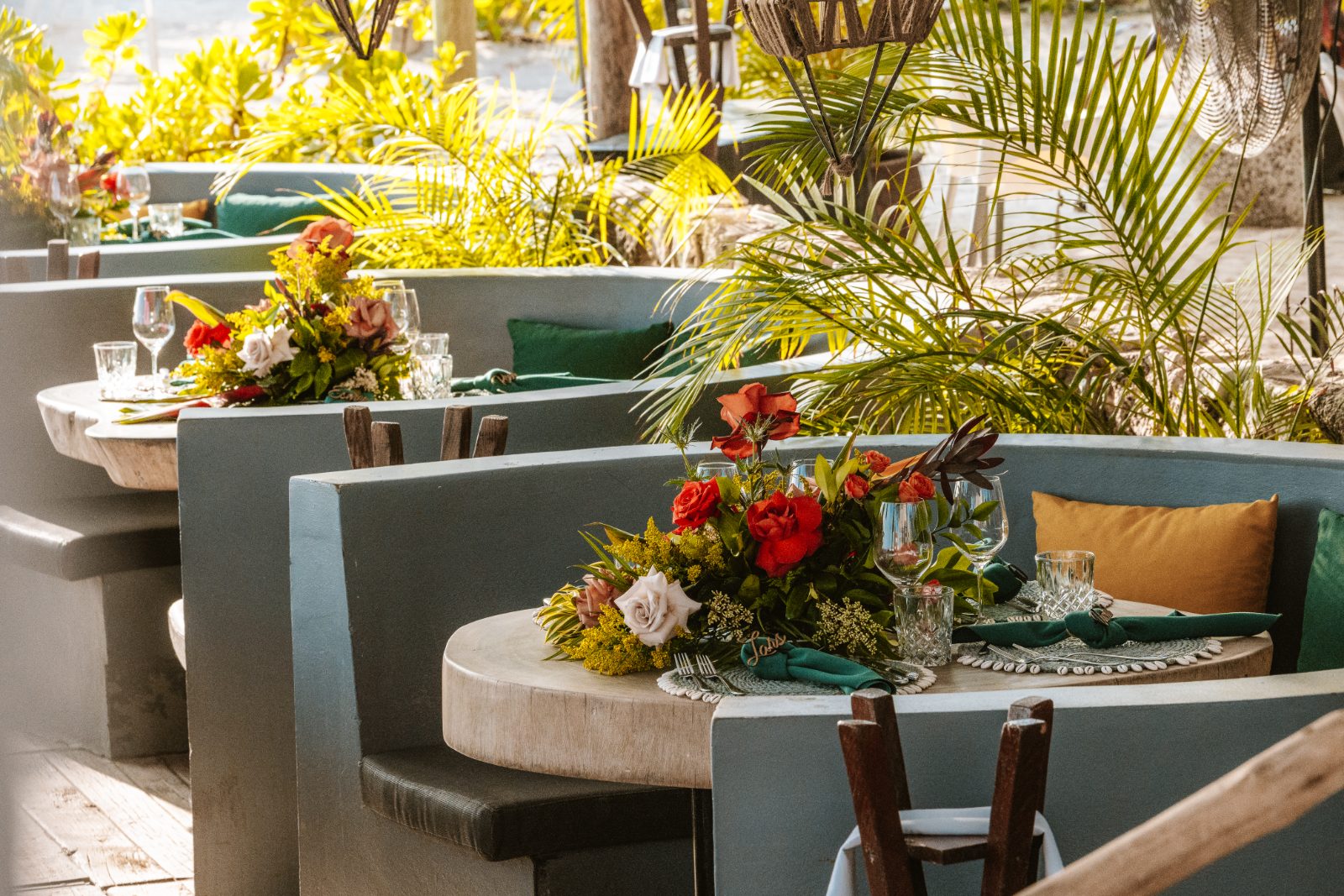 Sharon and Robin's wedding reception is set at MOOD Beach in Curaçao, featuring decorated tables with floral centerpieces and tropical greenery
