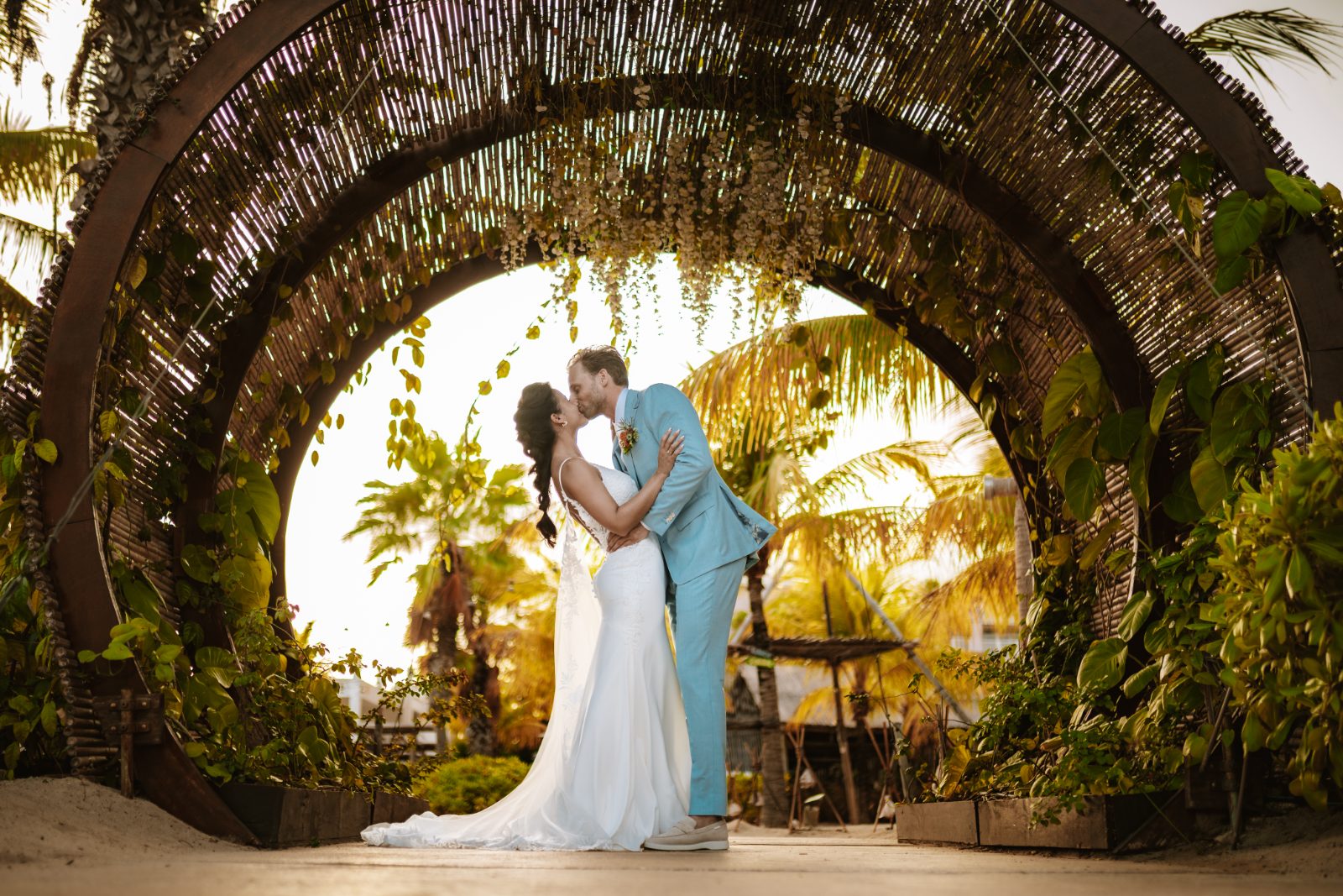 Sharon and Robin kiss at their wedding ceremony in an archway surrounded by greenery at MOOD Beach, Curaçao