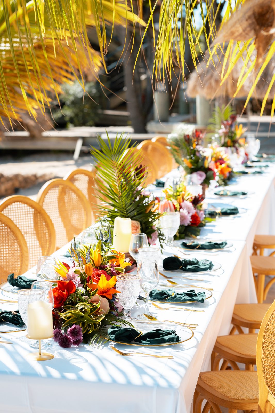 Stephanie and Simon's wedding reception is set at Avila Beach Hotel, Curaçao, featuring a decorated long dining table surrounded by tropical plants