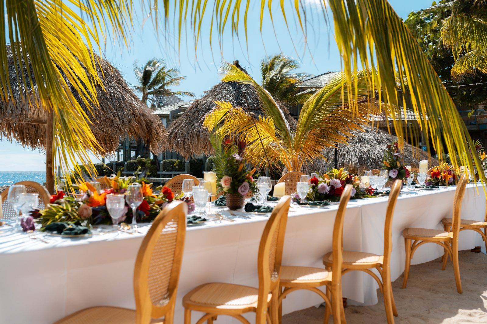 Stephanie and Simon's wedding reception features a long table decorated with flowers and settings, set outdoors at Avila Beach Hotel in Curaçao