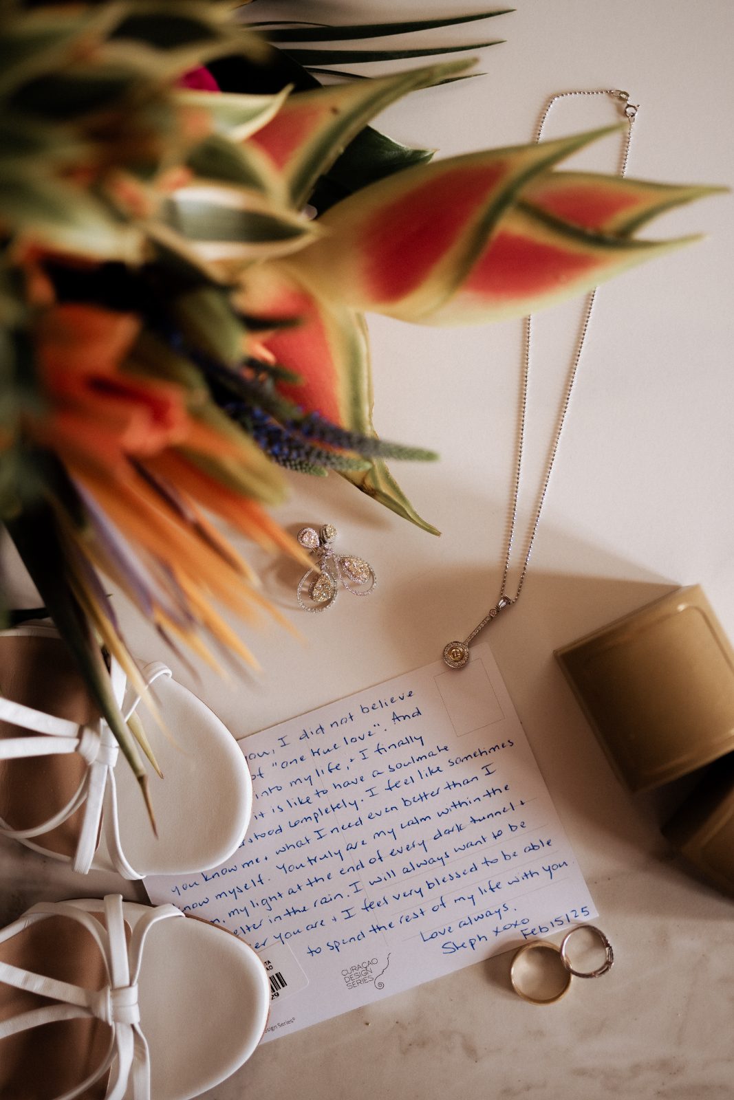 Stephanie and Simon's wedding items are arranged on a surface at Avila Beach Hotel, featuring a letter, jewelry, and sandals
