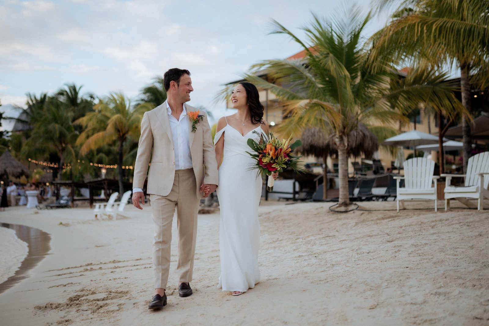 Stephanie and Simon are walking hand in hand along the beach at Avila Beach Hotel in Curaçao, surrounded by palm trees